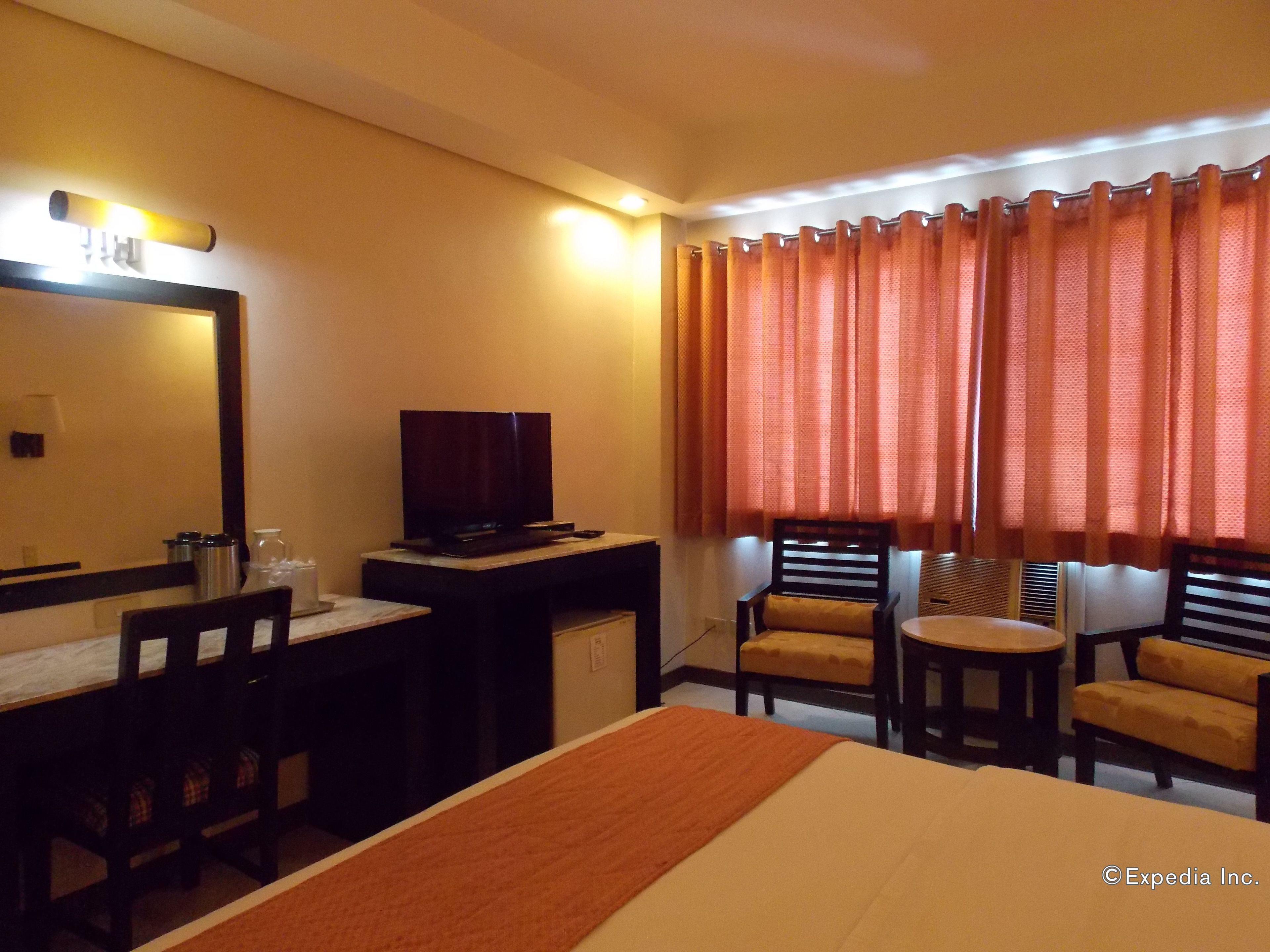 A hotel room with a bed, a desk with a television, two chairs, and a window with curtains.