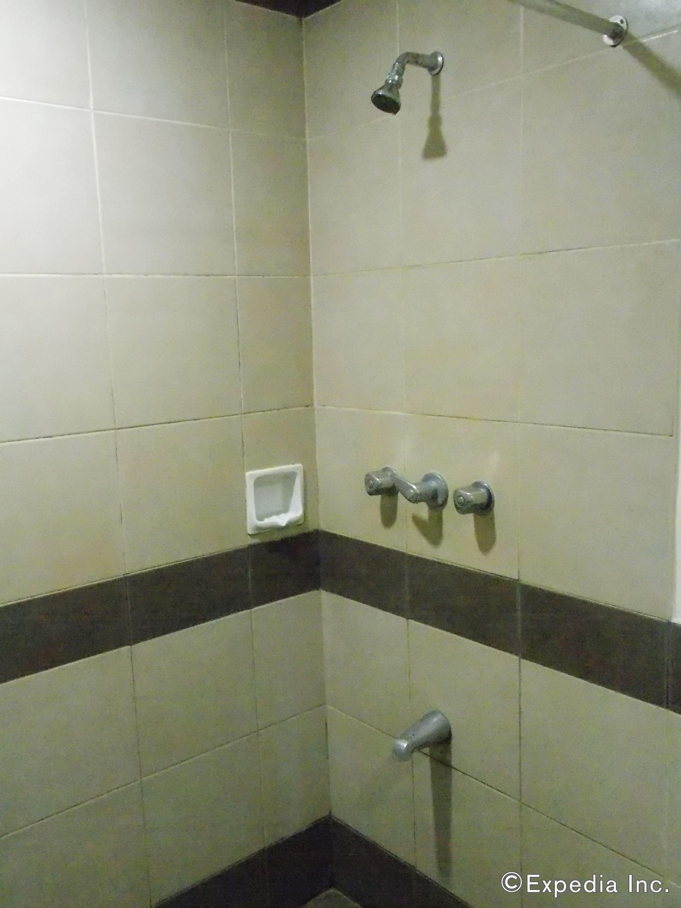 A bathroom with white and dark brown tiles, a showerhead, a soap dispenser, and a toilet paper holder.