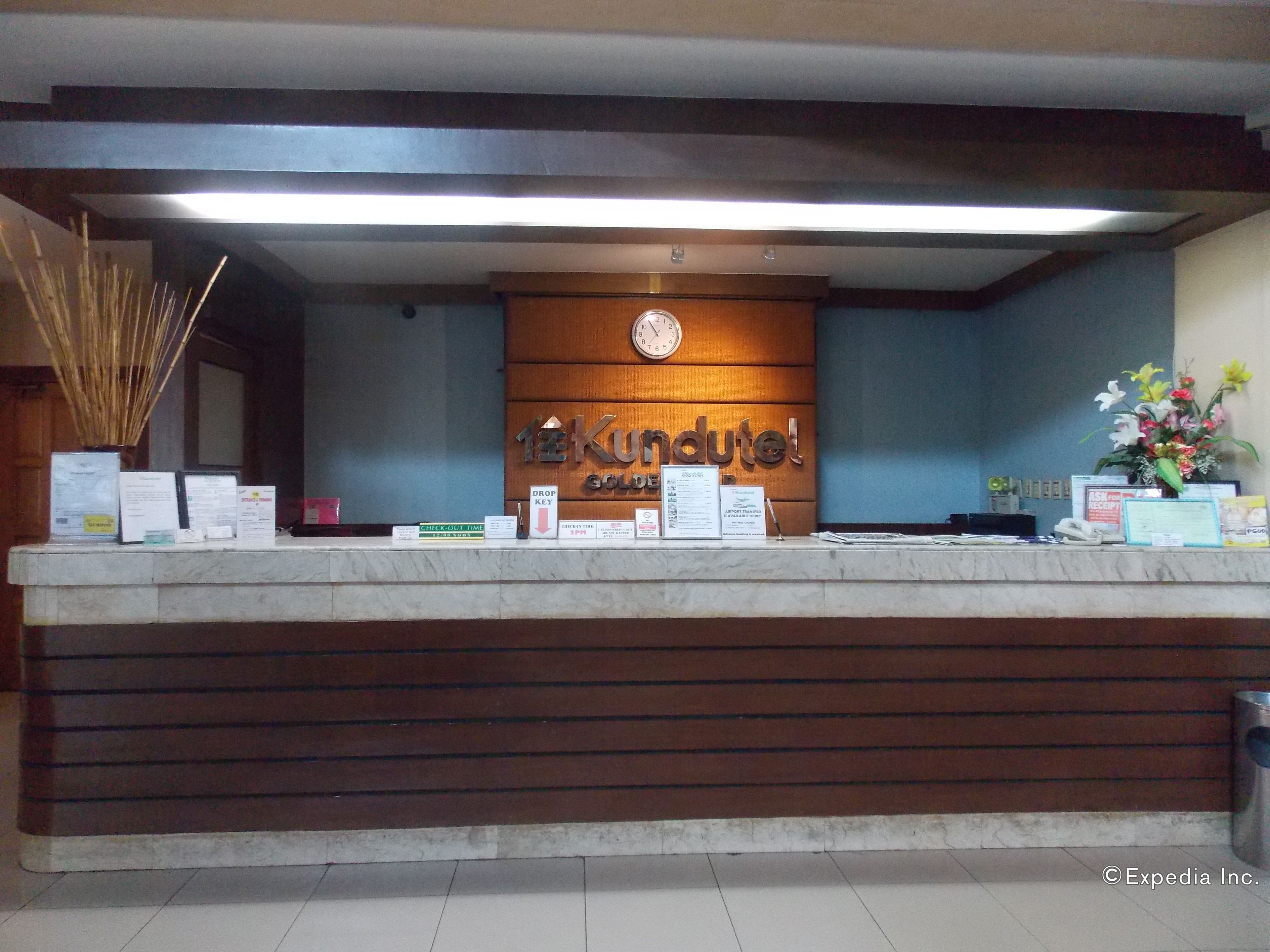 A hotel reception desk with a wooden panel design, a clock, and various informational signs.