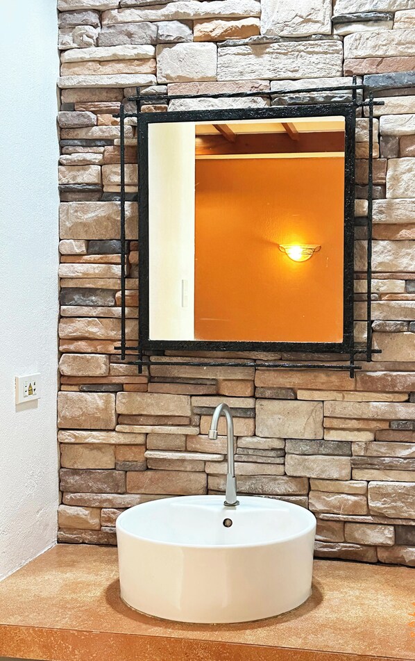 A bathroom with a stone wall, a white sink, and a mirror with a black frame.