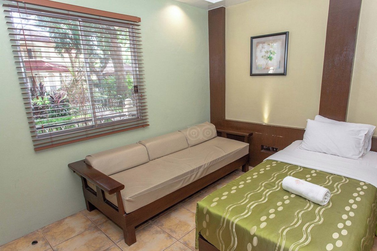Um quarto com uma cama, um sofá, uma janela com persianas e um quadro na parede.