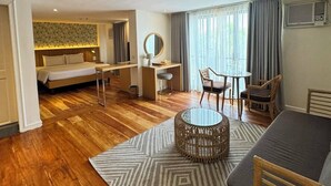 Habitación de hotel con piso de madera, una cama, un escritorio, una mesa de centro redonda de mimbre y un sofá.