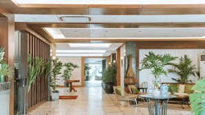 Un vestíbulo amplio con techos altos, mobiliario moderno y abundante vegetación de interior.