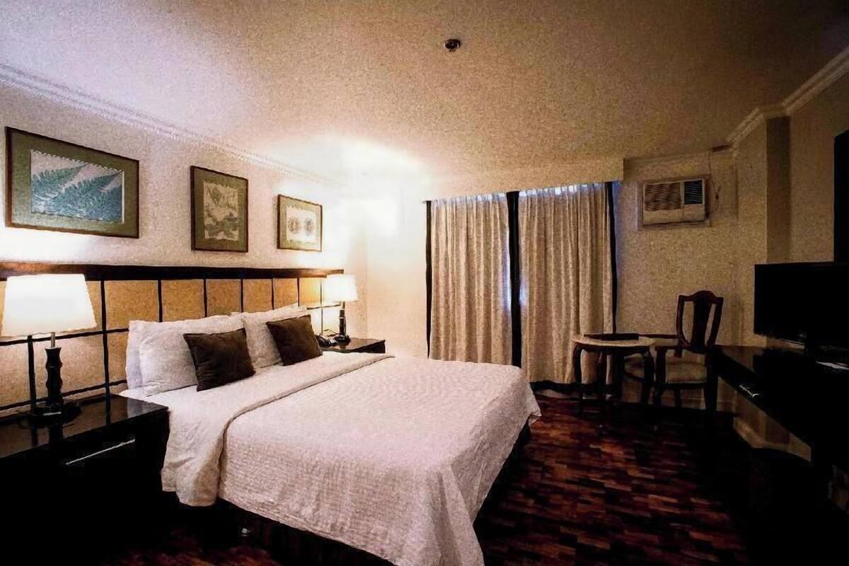 Une chambre d’hôtel comprenant un lit, des tables de chevet, une chaise, un bureau et un téléviseur.