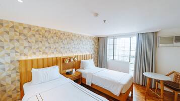 Habitación de hotel con dos camas, cabecero de madera, una mesita y una ventana con cortinas.