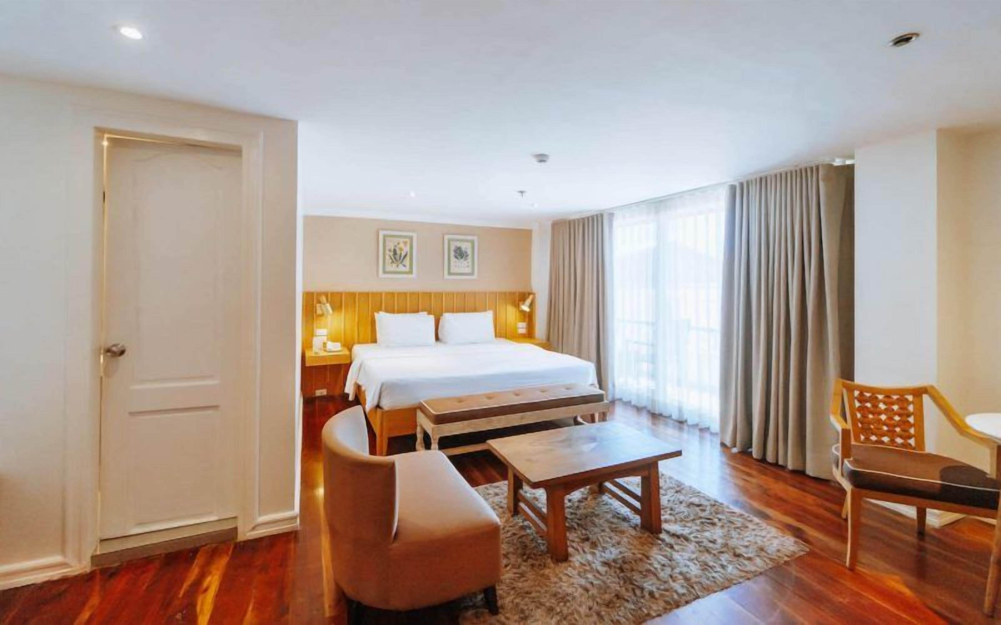 A hotel room with a large bed, a desk, a chair, and a window with curtains.
