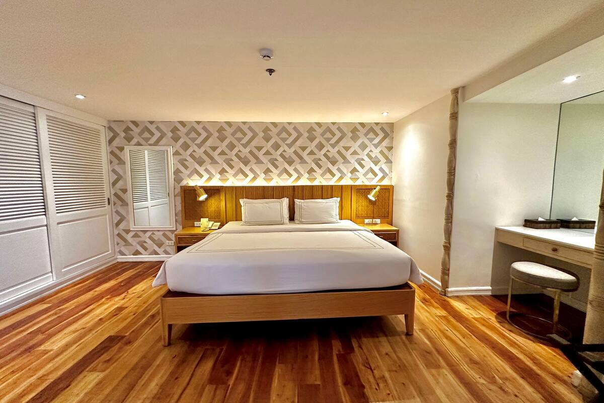 Une chambre moderne avec un lit en bois, une table de chevet avec une lampe, une coiffeuse avec un miroir et une fenêtre avec des stores.