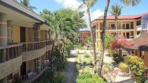 A multi-story hotel with balconies, palm trees, and a courtyard. - Bamboo Beach Resort and Restaurant (Balabag)