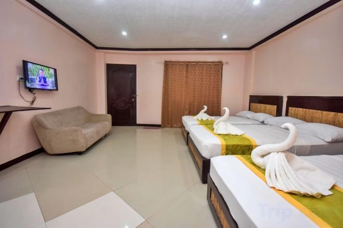 Habitación de hotel con sofá, dos camas con toallas formando cisnes, un televisor y una puerta.