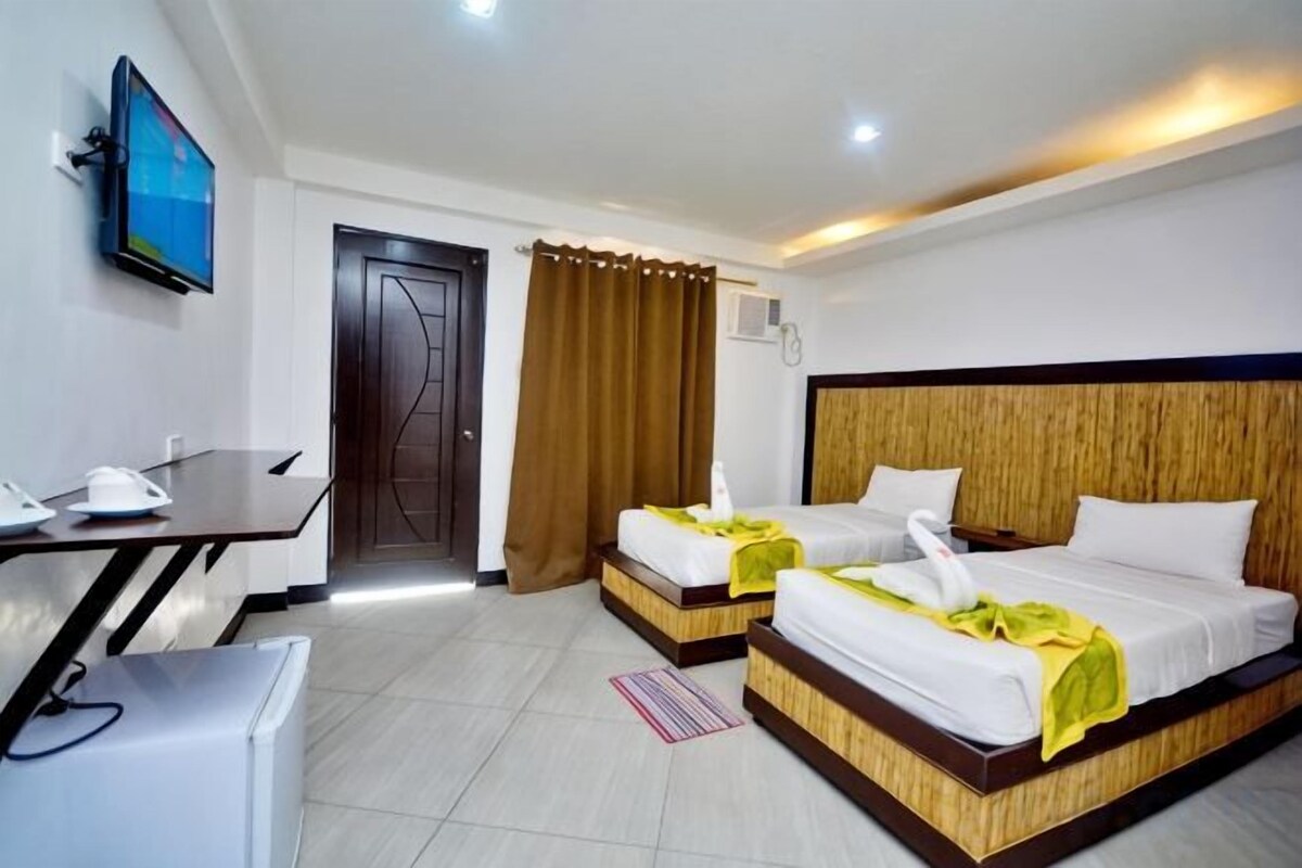 Habitación de hotel con dos camas, un escritorio, un televisor y una puerta.