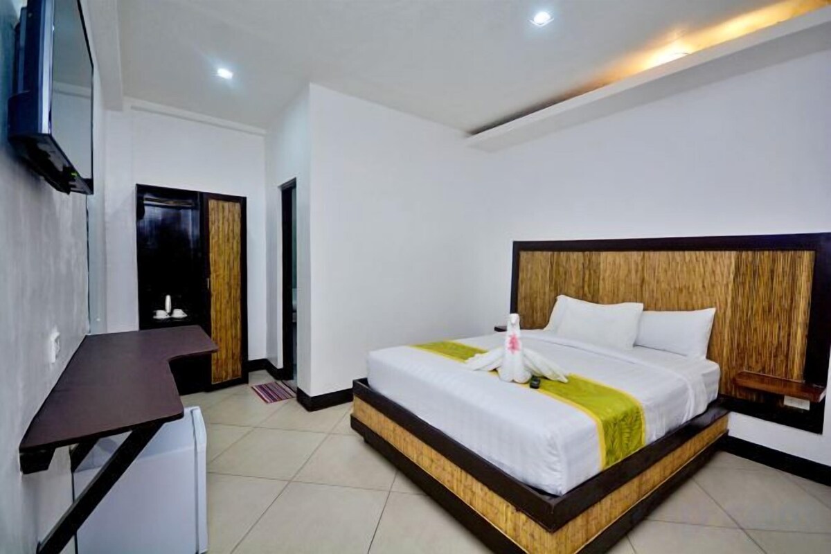 Habitación de hotel con cama, mesita de noche y televisor montado en la pared.