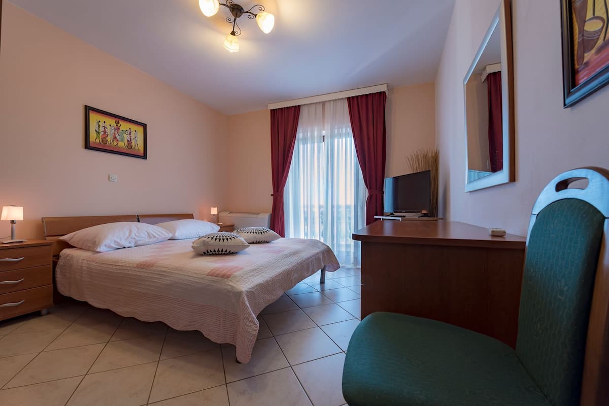 Quarto de hotel com cama, escrivaninha, cadeira, televisão e um quadro na parede.