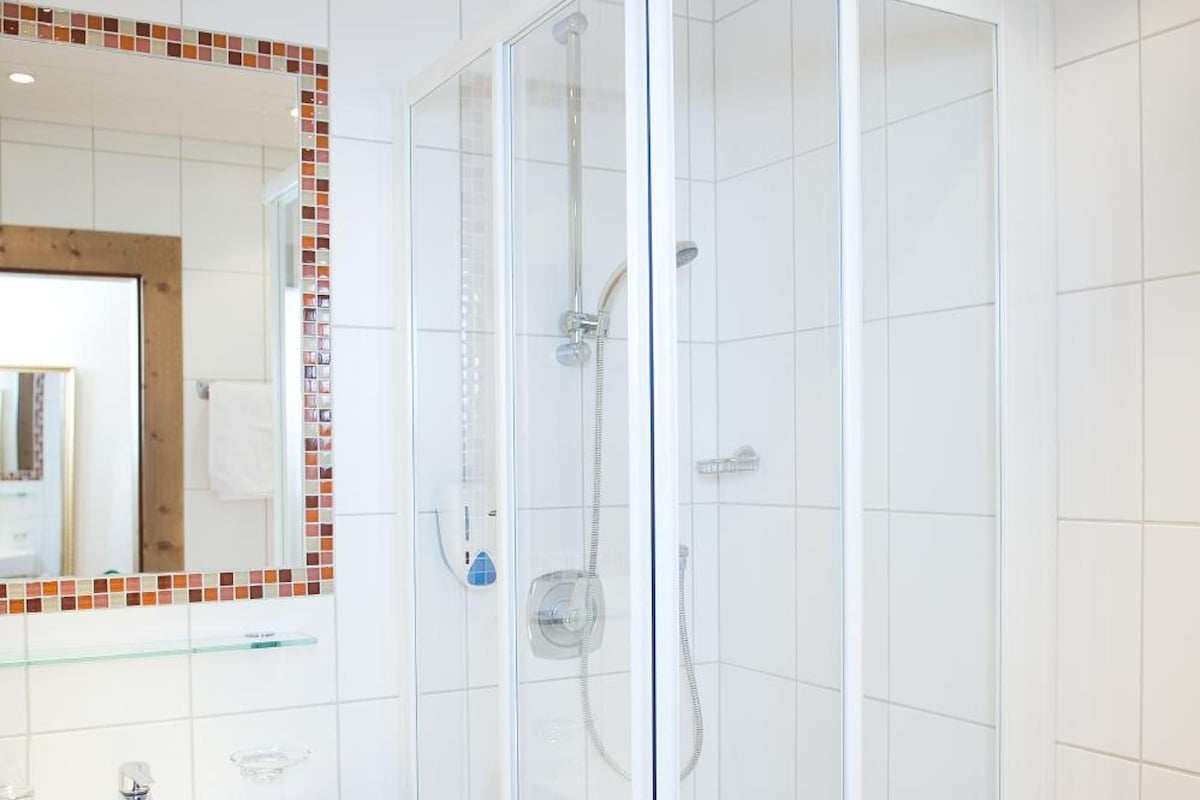 Une salle de bain avec une douche à parois de verre, un lavabo blanc et un mur recouvert de carreaux.
