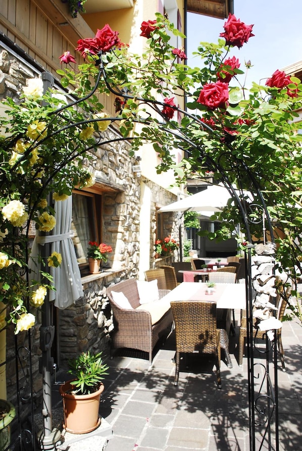 An outdoor seating area with wicker furniture, a stone wall, and a pergola with climbing roses.