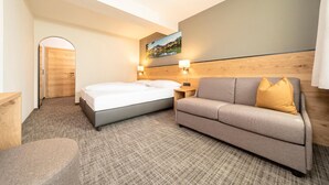 Une chambre d’hôtel avec un lit, un canapé, une table de chevet et un tableau au mur.