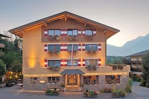 A hotel with a restaurant-bar at the ground level, multiple windows with shutters, and flower boxes on the balconies.