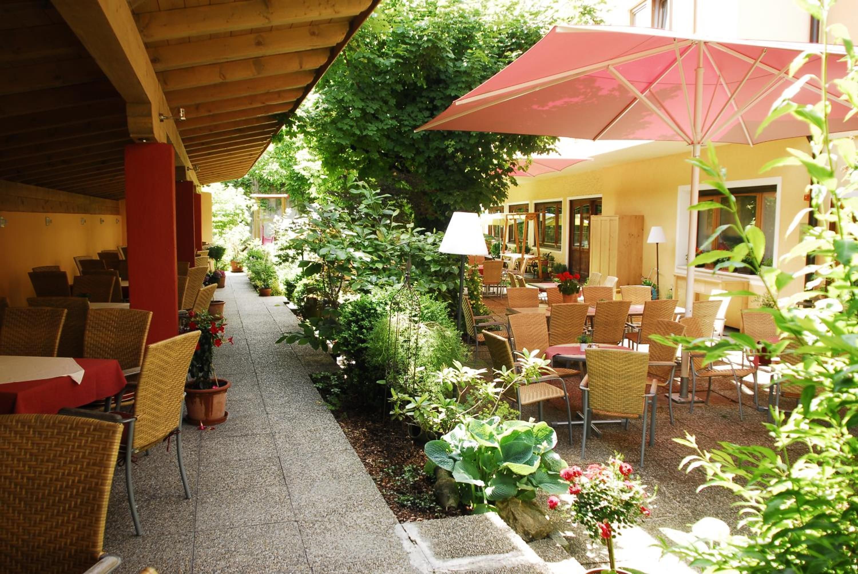 An outdoor seating area with wicker chairs and tables, surrounded by greenery and potted plants.