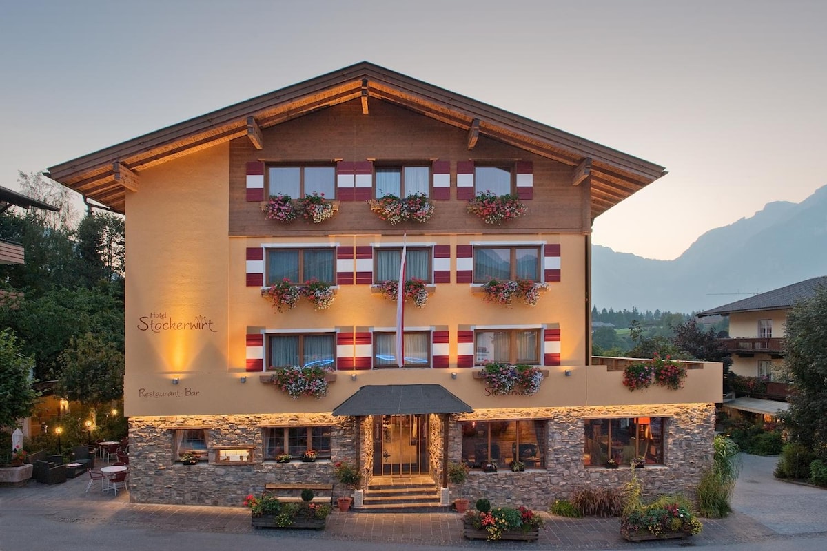 Un hôtel à plusieurs étages, doté d’une façade en pierre, de balcons ornés de jardinières et d’un restaurant-bar situé au rez-de-chaussée.