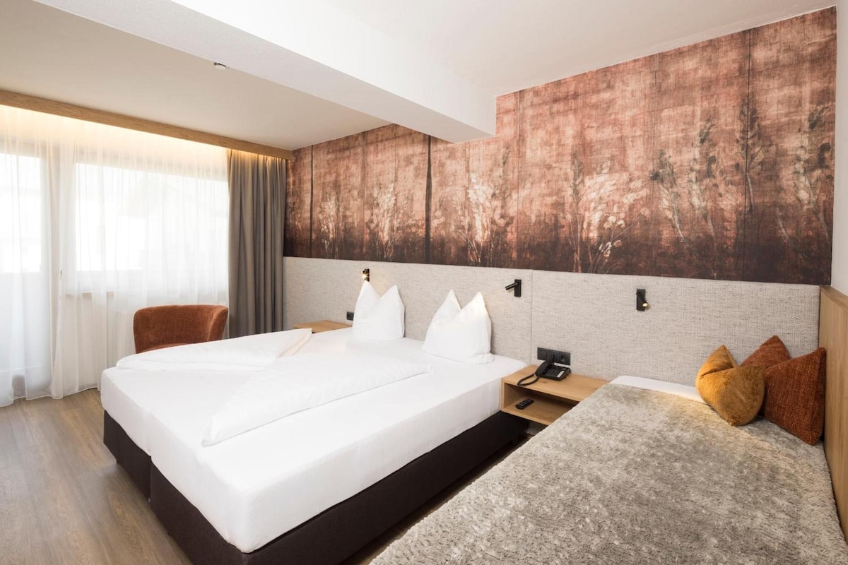 A modern hotel room with a large bed, a smaller sofa, a desk with a phone, and a large abstract wall art piece.