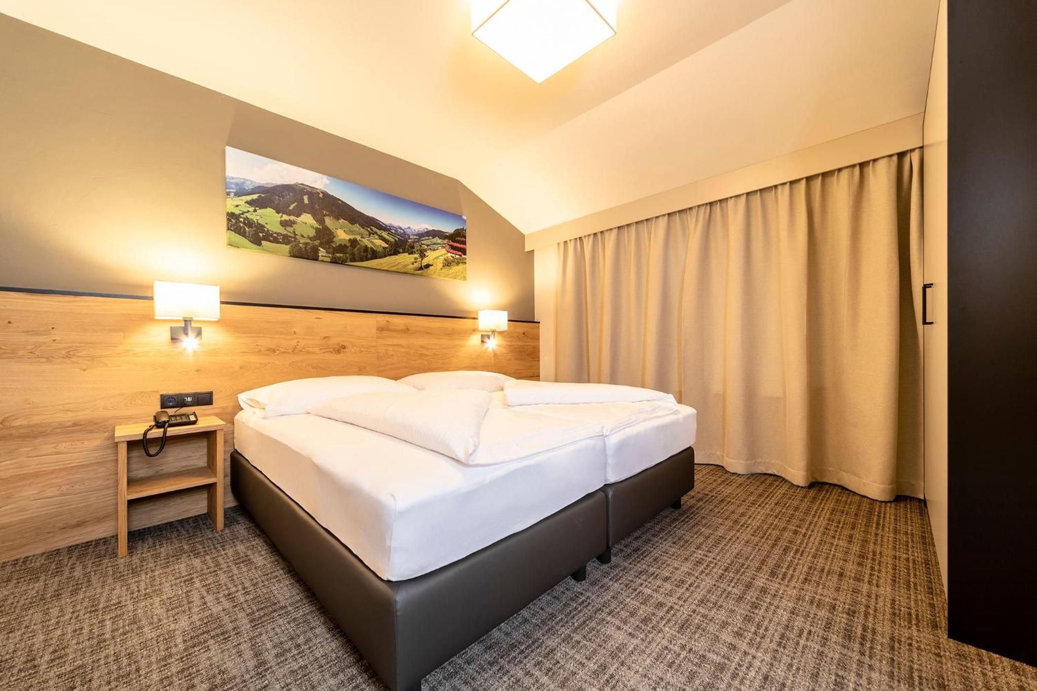 Habitación de hotel con una cama grande, una mesita de noche con una lámpara, un cuadro en la pared y vistas al exterior.