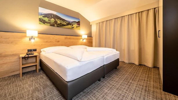 Une chambre d’hôtel avec un grand lit, une table de chevet avec une lampe, un tableau au mur et une vue sur l’extérieur.