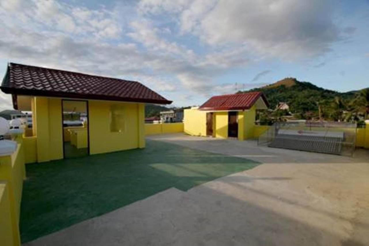 Un edificio amarillo con tejado rojo, una zona con techo verde y vistas a una colina al fondo.