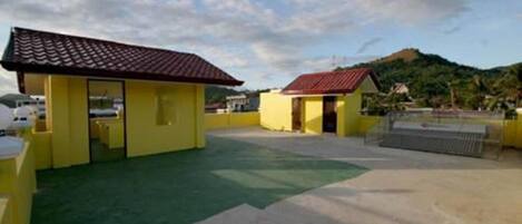 Un edificio amarillo con tejado rojo, una zona con techo verde y vistas a una colina al fondo.