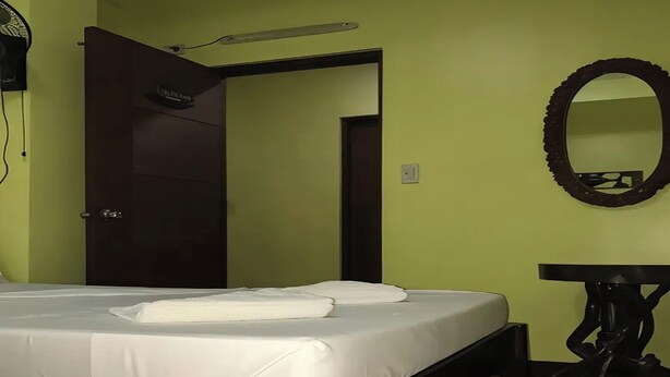 A hotel room with a bed, a bedside table, a mirror, and a door leading to another room. - Luis Bay Travellers Lodge Coron (Coron)