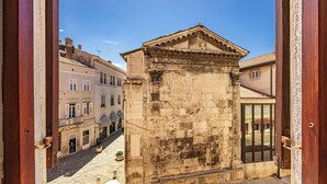 A view from a window overlooking a historic building with a classical facade, a cobblestone street, and adjacent buildings. - Diana City Hall View (Pula)