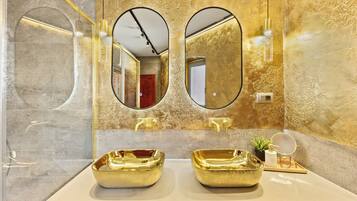 Une salle de bain avec deux lavabos dorés, un grand miroir et une petite plante en pot.