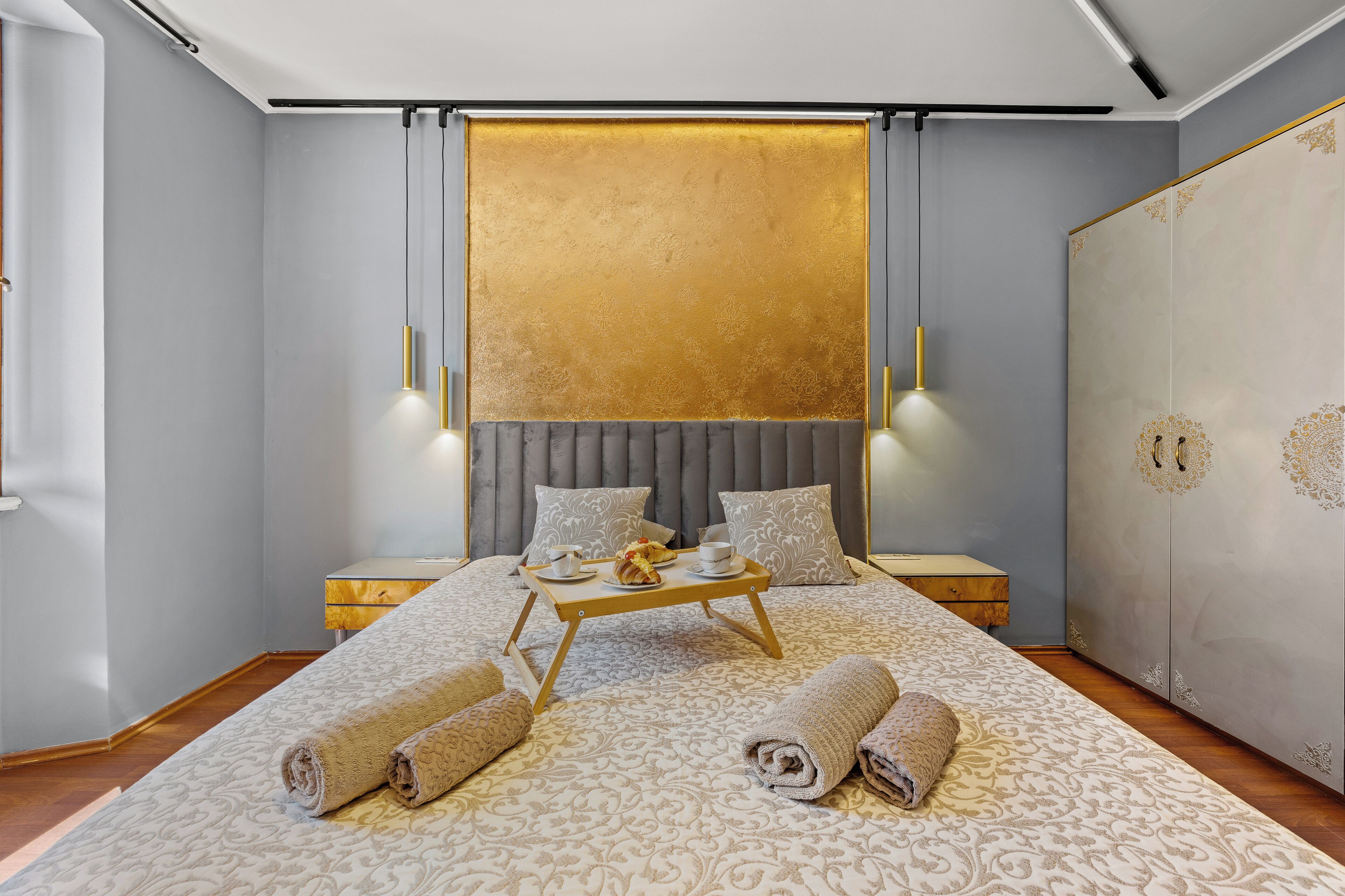 A modern hotel room with a large bed, a bedside table, a wardrobe, and a golden accent wall.