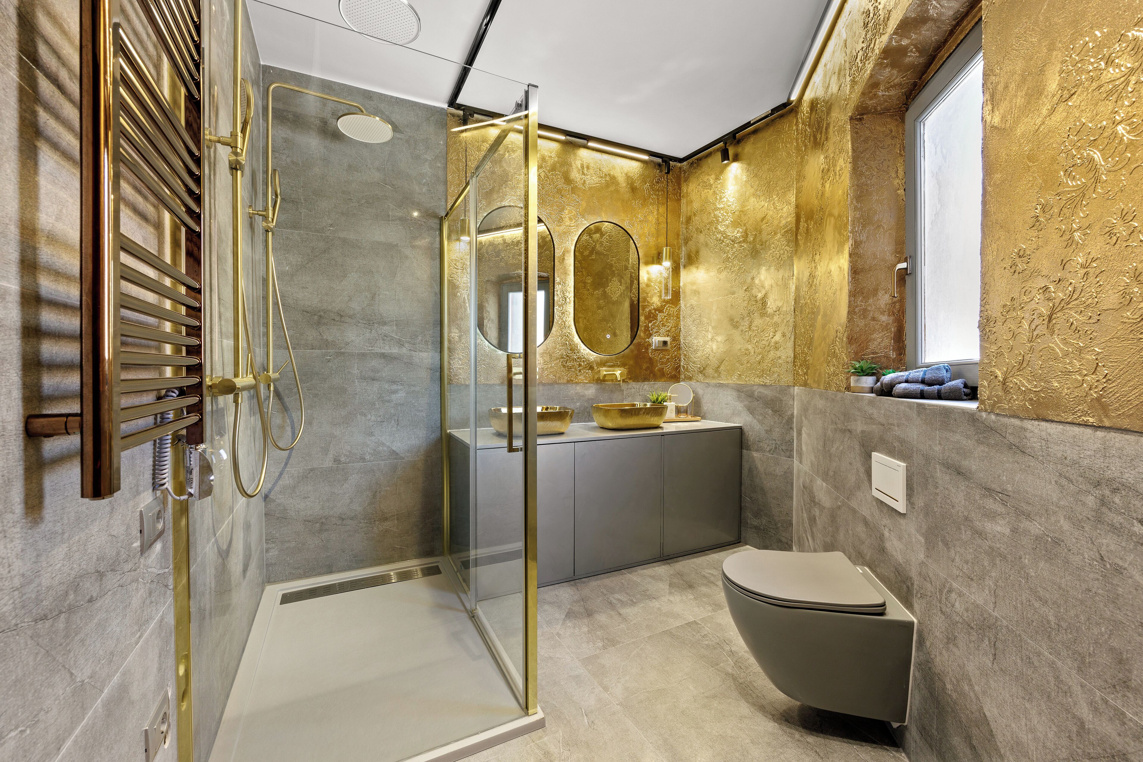 Un bagno moderno con cabina doccia in vetro, un mobile lavabo con finitura dorata e un grande specchio.