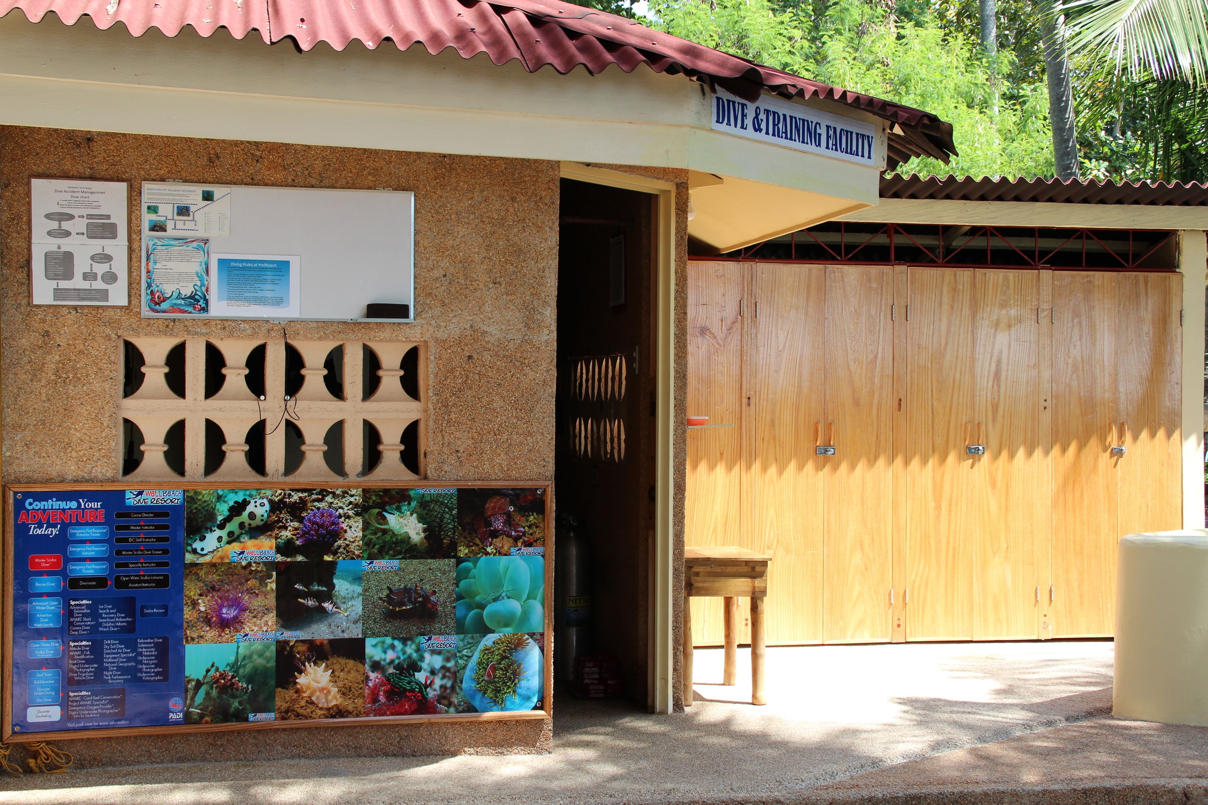 A dive and training facility with a wooden door, a bulletin board with marine life photos, and a small table outside.