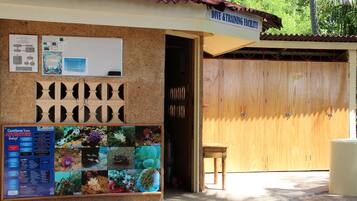A dive and training facility with a wooden door, a bulletin board with marine life photos, and a small table outside.