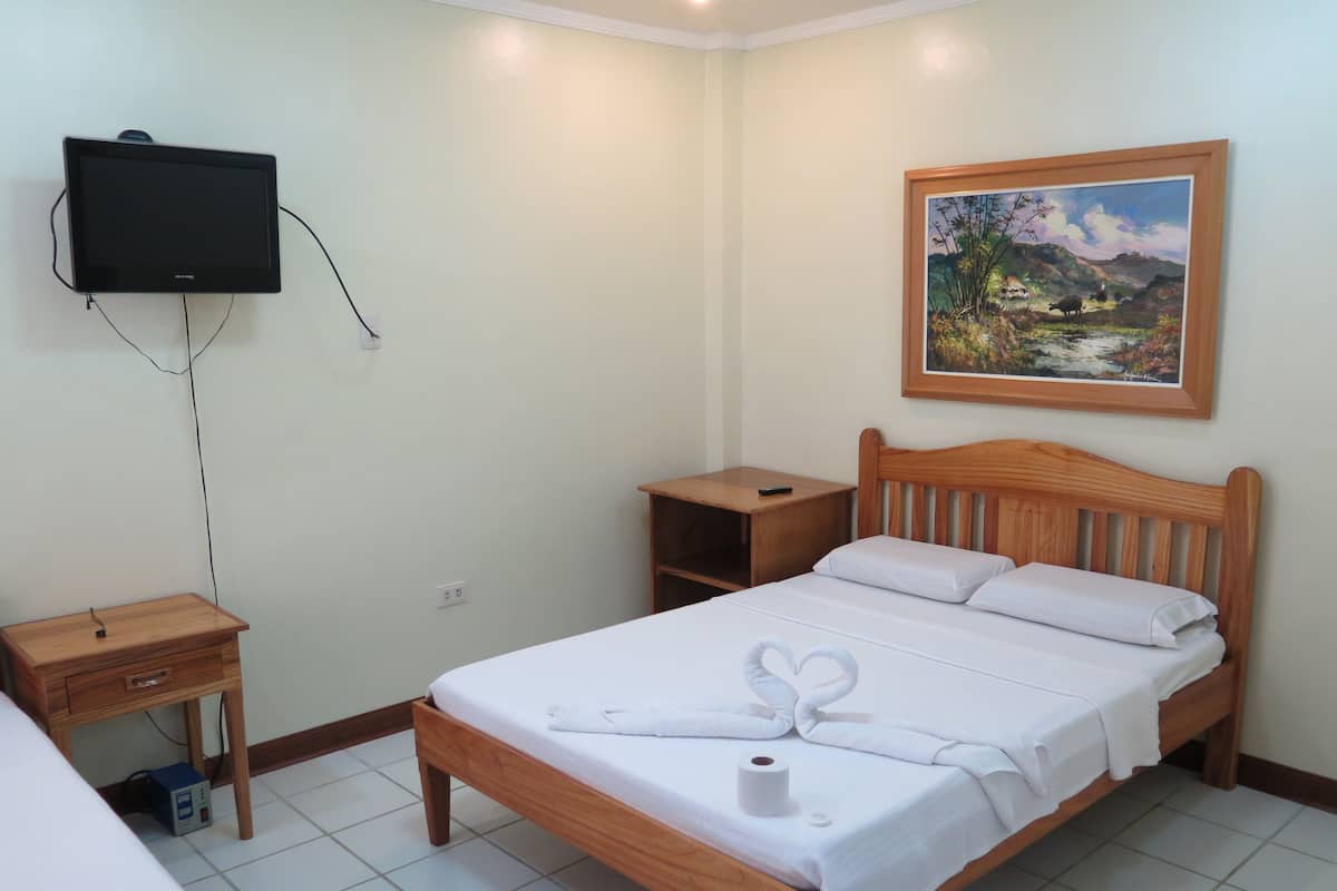 A neatly arranged bedroom with a bed, a bedside table, a TV mounted on the wall, and a painting above the bed.