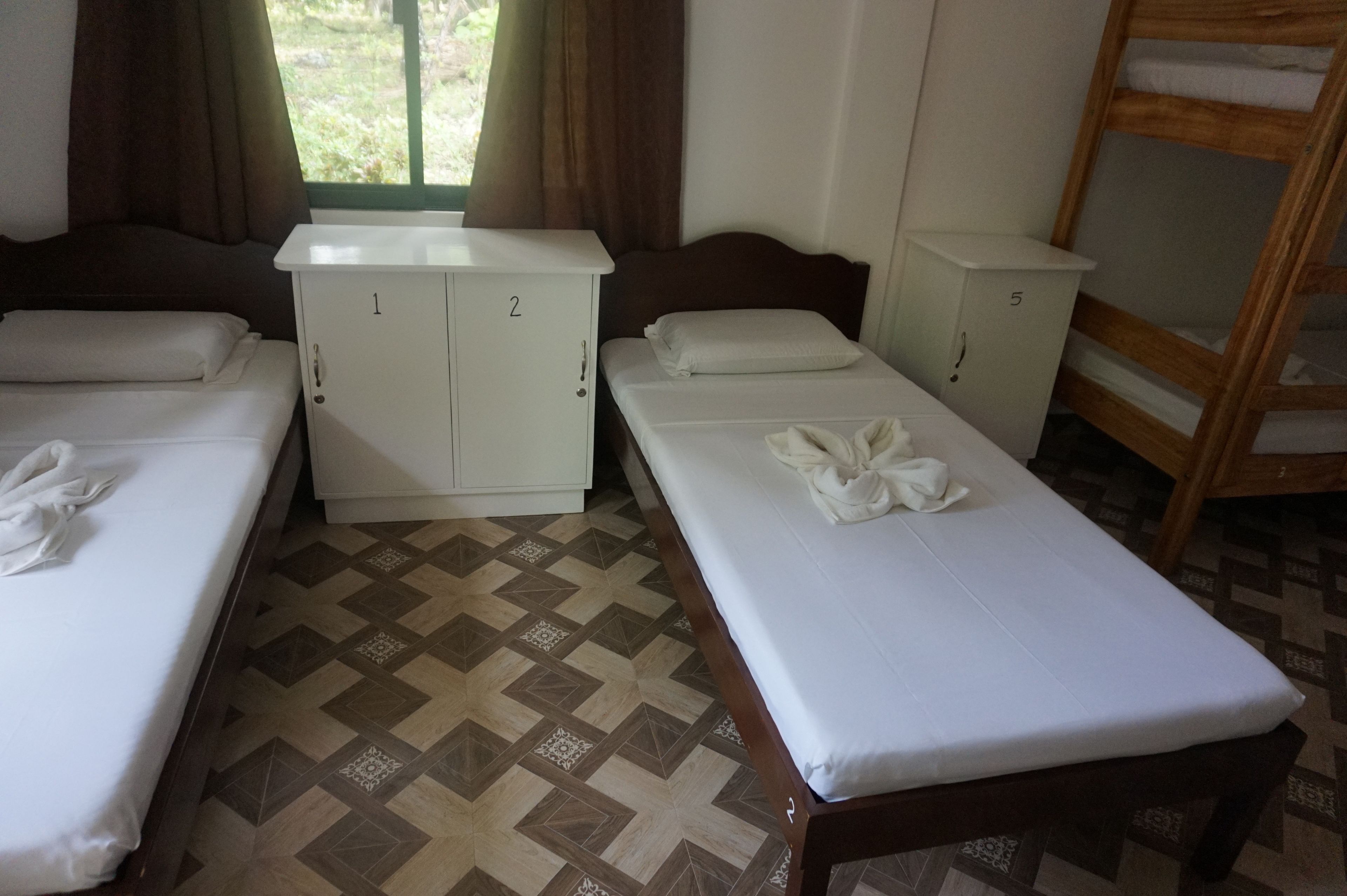 Ein Hotelzimmer mit zwei Betten, darunter ein Etagenbett aus Holz, einem Fenster mit Vorhängen und einem gemusterten Boden.