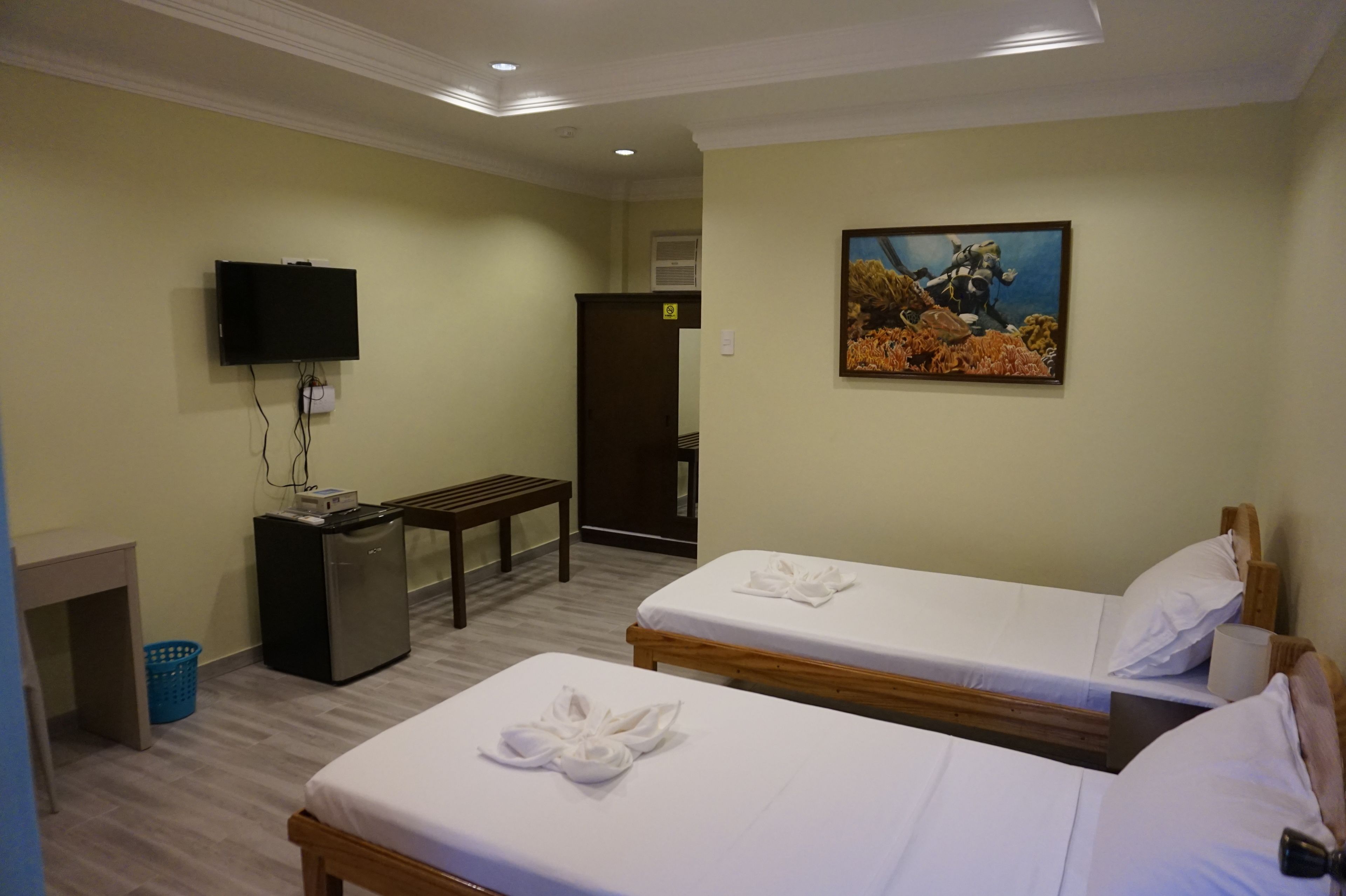 A hotel room with two beds, a desk, a television, a painting, and a small refrigerator.
