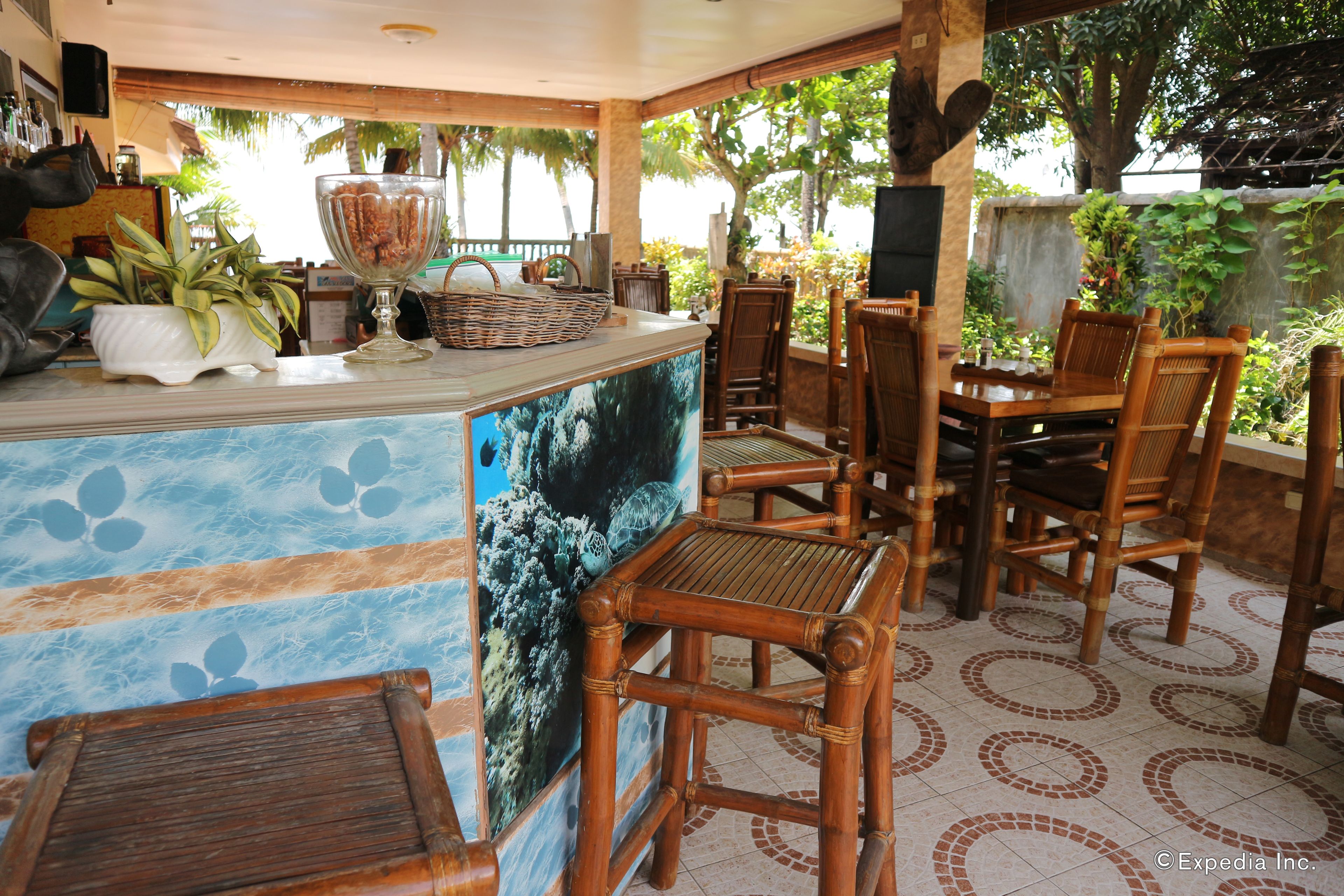 A restaurant with a wooden bar, wicker chairs, and a tiled floor with a circular pattern.