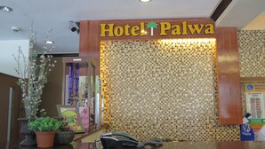 Un mostrador de recepción con un cartel que dice "Hotel Palwa" y una pared de mosaicos al fondo.