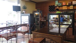 Un interior de restaurante con sillas de mimbre, una mesa grande, un refrigerador y estantes con bebidas.