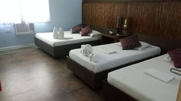 Habitación de hotel con dos camas, cada una con ropa blanca y almohadas, cabeceros de madera, mesitas de noche pequeñas con lámparas y una ventana con cortinas.