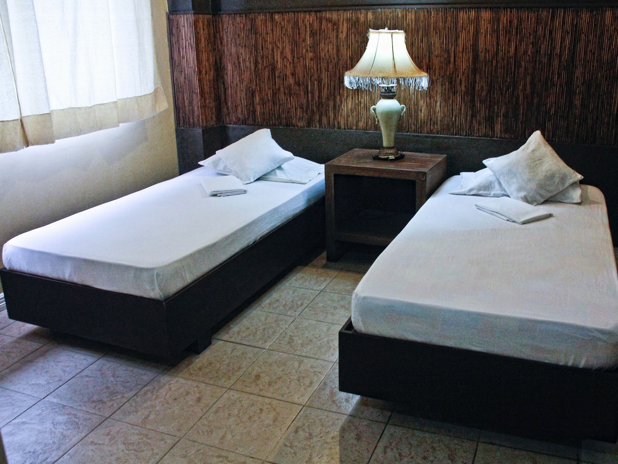 Une chambre d’hôtel avec deux lits simples, une table de chevet et une lampe.