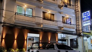 Un hotel de varios pisos con balcones, un letrero de restaurante a la vista y un vehículo estacionado.