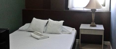 Una cama bien hecha con almohadas y una toalla doblada, una lámpara de noche y una mesita auxiliar en una habitación de hotel.