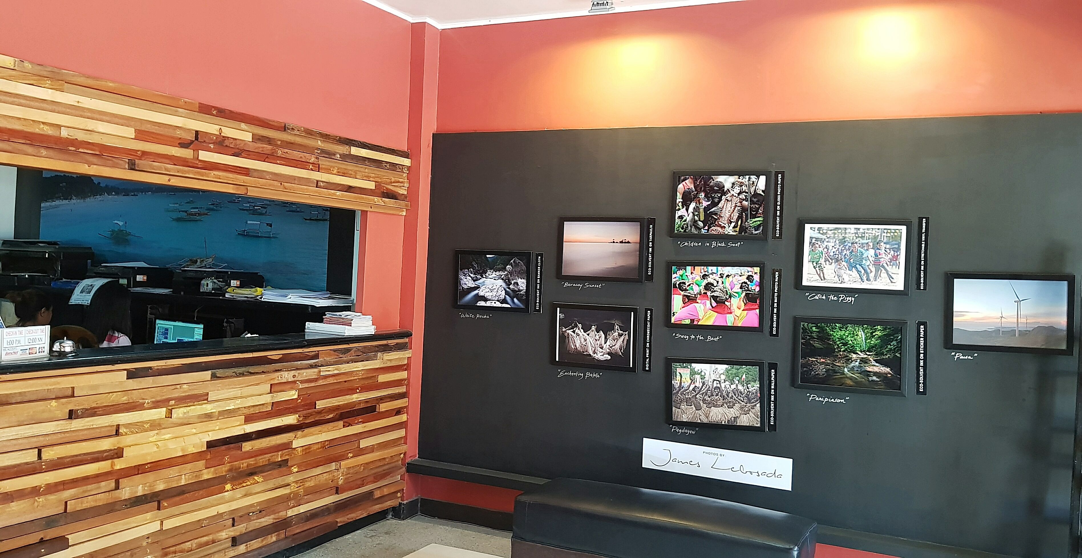 Zona de recepción con un mostrador de madera, una gran pantalla de televisión mostrando una vista panorámica y una pared decorada con cuadros enmarcados.