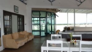 A modern living room with a beige sofa, a dining table with white chairs, and a large glass door leading to a balcony with a view. - Ace Penzionne (Lapu-Lapu)