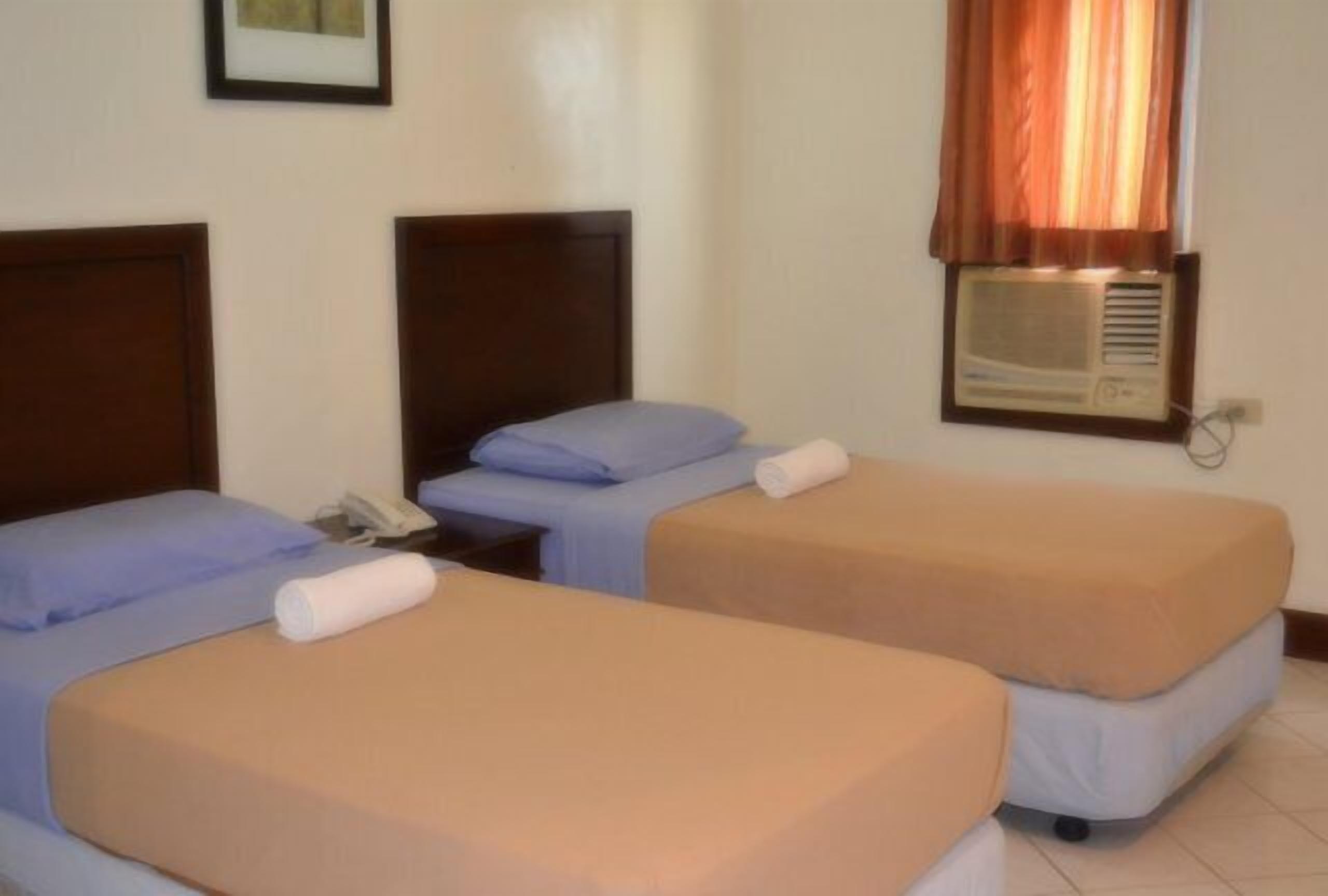 A hotel room with two single beds, a bedside table with a phone, and a wall-mounted air conditioner.