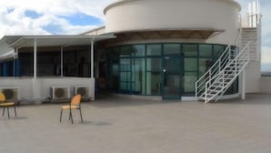 A modern building with a curved glass facade, outdoor seating area with chairs, and a staircase leading to an upper level. - Ace Penzionne (Lapu-Lapu)