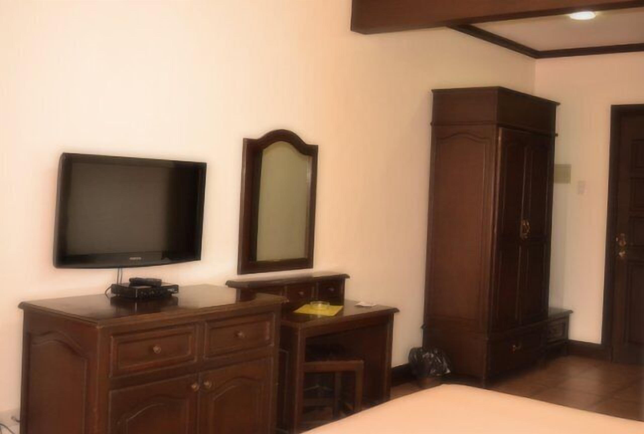 A bedroom with a bed, a TV, a dresser, a mirror, and a wardrobe.