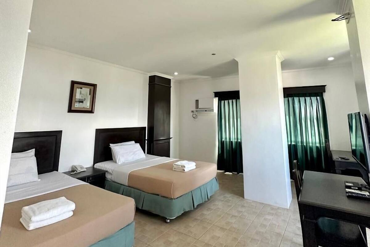 A hotel room with two beds, a desk, a television, and a bathroom visible through an open door.